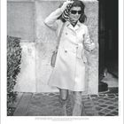 Jackie Kennedy Onassis in elegantem Mantel und Stiefeln, hält sich ein Halstuch fest, dunkel getönte Sonnenbrille.