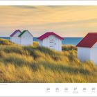 Mai-Kalender: Strandhütten in Gouville-sur-Mer, Frankreich. Weiße Hütten mit bunten Dächern in Dünen, Meer im Hintergrund.