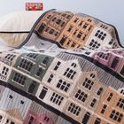 "Knit Your City" auf rotem Spielzeugbus. Decke mit gestricktem Stadtmotiv in verschiedenen Farben auf einem Bett.