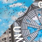 Text: „UMBE“. Zahlreiche Vögel fliegen vor einem blauen Himmel. Architektur mit gläsernem Dachmuster und klassischen Details.