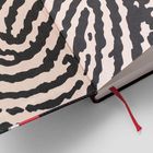 Ein geöffnetes Buch mit einem schwarz-weißen Muster, das an Fingerabdrücke erinnert. Ein rotes Stoffbändchen als Lesezeichen.
