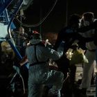 Verschwommener arabischer Text auf einem Schild. Menschen in Schutzanzügen interagieren mit einer Menschenmenge bei Nacht.