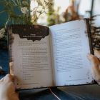 Übung: "Reise in ein früheres Leben". Anleitung zur Meditation. Hände halten das Buch. Im Hintergrund Pflanzen.