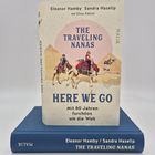 Buchcover: "The Traveling Nanas", "Here We Go", zwei Frauen auf Kamelen vor Pyramiden, beige Hintergrund, blaues Buch.