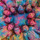 Kinder liegen im Kreis am Boden, bedeckt mit buntem Puder in lebendigen Blau-, Pink- und Grüntönen.