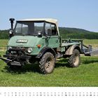 Text: "APRIL", Kalendertage und -daten. Grüner Unimog auf einer Wiese, mit Anbaugerät hinten, Hintergrund Wald.