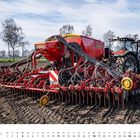 Der Text "APRIL" steht unter einem Kalender. Traktor mit roter Sämaschine auf einem Acker, Bäume im Hintergrund.