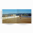 Wand mit Werbetexten, staubiger Fußballplatz, Person in der Mitte, umgeben von Hügeln und klarem Himmel.