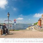 Fähre “Rääße Pöntje.” April 2027. Skulpturen eines sitzenden und stehenden Mannes an der Rheinpromenade, nahe Wasser und Brücke.