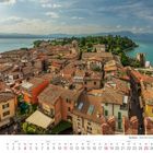 Kalenderbild von April 2027, zeigt Sirmione am Gardasee mit roten Dächern, alter Architektur, grünem Ufer und blauem Wasser.