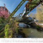 "Wuppertaler Schwebebahn - Station Ohligsmühle", Kalender für April 2027. Schwebebahn über Fluss, blühender Baum, modernes Gebäude.