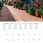 Kalenderblatt für November mit Wochentagen in mehreren Sprachen. Kopfsteinpflasterstraße mit blühenden Pflanzen.