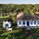 Ein traditionelles Haus mit blauen Fenstern und Türen, umgeben von Palmen. Zwei Personen mit zwei Pferden im Garten.