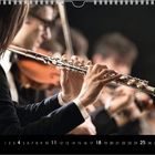 Kalenderblatt für April, Flötist in Orchester, Fokus auf Hände und Instrument, Hintergrund unscharf, klassische Atmosphäre.