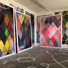 Verschiedene Werke zeigen bunte Rautenmuster in einem Atelier mit skizzierten Linien am Boden.