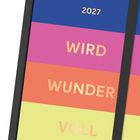 2027 wird wundervoll. Bunte Streifen in Blau, Pink, Orange und Gelb auf einem Kalender.