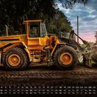 Kalender mit Monatsübersicht. Ein großer gelber Bagger steht auf einer Baustelle bei Sonnenuntergang.