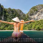 Kalender April: Eine Frau in Bademode und Sonnenhut steht mit ausgebreiteten Armen auf einem Boot vor tropischen Felsen.