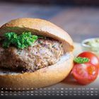 Kalender mit April-Daten. Ein Brötchen mit Frikadelle und Petersilie, daneben Tomaten und ein Schälchen Dip.