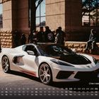 Text unten: "Chevrolet Corvette 9" und Kalender. Ein weißer Sportwagen steht auf einer sonnigen Straße. Im Hintergrund Leute und Gebäude.