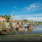 Kalender mit Hafenszene in Greetsiel, Schiffe im Wasser, rote Ziegeldächer, blauer Himmel, grünes Ufer.