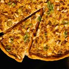 Ein Stück Tarte oder Quiche mit Zwiebeln, Frühlingszwiebeln und Pinienkernen auf dunklem Hintergrund.