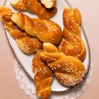 Es gibt keinen Text. Auf einem Teller liegen geflochtene, mit Zucker bestreute Backwaren auf einer rosafarbenen Tischdecke.