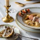 Ein feierlich gedeckter Tisch mit brennender Kerze, Sektglas, Austern auf Teller und Bouillon mit Fleisch und Garnelen.