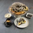 Mohnkuchen auf einer Tortenplatte, Sahne in einer Schüssel, Espresso in einer Tasse, Mohn in einem Quadratbehälter.