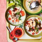 Suppenteller mit Kokosmilch-Suppe, Hühnchen, Kräutern. Limetten und Koriander daneben, rote Schale mit Chili.