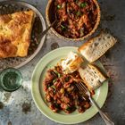 In einer grünen Schale befinden sich Ratatouille und Brot. Daneben ein Glas Wasser und ein Metallkorb mit Focaccia.