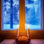 Keine sichtbaren Texte. Vier Kerzen in einem roten Adventskranz brennen auf einem Tisch, draußen ist es verschneit.