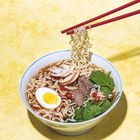 Keine Texte vorhanden. Schale mit Ramen, Ei, Fleisch, Spinat und Pilzen in Brühe. Rote Essstäbchen fassen Nudeln.