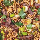 Nudeln mit gebratenem Fleisch, Frühlingszwiebeln, Chilis, Koriander und Soße in einer farbenfrohen Mischung.