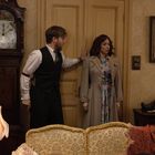 Ein Mann und eine Frau stehen in einem Wohnzimmer vor einer geschlossenen Doppeltür, umgeben von antiker Einrichtung.