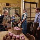 Eine Familie in einem gemütlichen, retro-stilvollen Raum mit eingemachten Gläsern auf dem Tisch. Eine Frau hält ein Kind.
