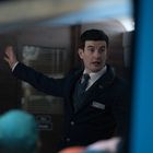 Ein Mann in Uniform gestikuliert mit offenem Mund. Im Hintergrund ein unscharfes Poster.