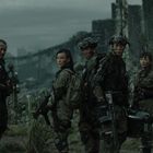 Fünf Personen in militärischer Ausrüstung stehen in einer zerstörten, bewachsenen Stadtlandschaft.