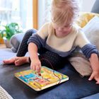 Ein Kind spielt konzentriert mit einem bunten, magnetischen Labyrinthspiel, während es auf einer Couch sitzt.