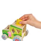 Holzspielzeugauto mit grünem Design, Schweinemotiv, eine Hand platziert einen gelben Zylinder oben.