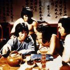 Chinesische Schriftzeichen auf Wand, fünf Männer sitzen um einen Tisch mit Teeutensilien, diskutieren konzentriert.