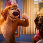 Ein Hund in einem Zimmer zeigt seine Muskeln vor einem Jungen. Im Hintergrund sind ein Fenster, ein Ventilator und Poster.