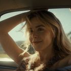 Es gibt keinen Text, der beschrieben werden kann. Eine Person sitzt im Auto und lächelt verträumt in den Sonnenschein.