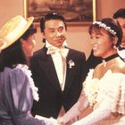 Vier Menschen in formeller Kleidung, zwei Frauen in Dialog, eine lächelt, ein Mann beobachtet, blumenverziert.