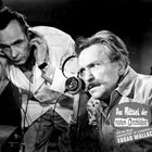 „Das Rätsel der roten Orchidee“ steht auf dem Mantel eines Mannes mit Kopfhörern. Beide Männer schauen ernst.