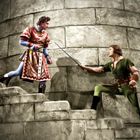 Zwei Männer in historischen Kostümen duellieren sich mit Schwertern auf einer Steintreppe.