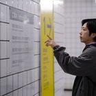 Schild mit Informationen auf Englisch und Japanisch; Mann zeigt darauf in einer gefliesten Umgebung.