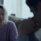 Eine Frau im lila Pullover schaut besorgt, ein Mann sitzt ihr nachdenklich gegenüber. Retro-Stereoanlage im Hintergrund.