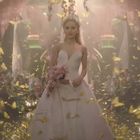 Eine Braut schreitet in einem weißen Kleid durch einen Raum voller goldener Schmetterlinge, mit Blumenschmuck auf dem Kopf.