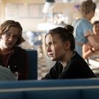 Zwei junge Menschen in einem Café, sitzen in blauen Sitzbänken, unterhalten sich, weitere Personen im Hintergrund.